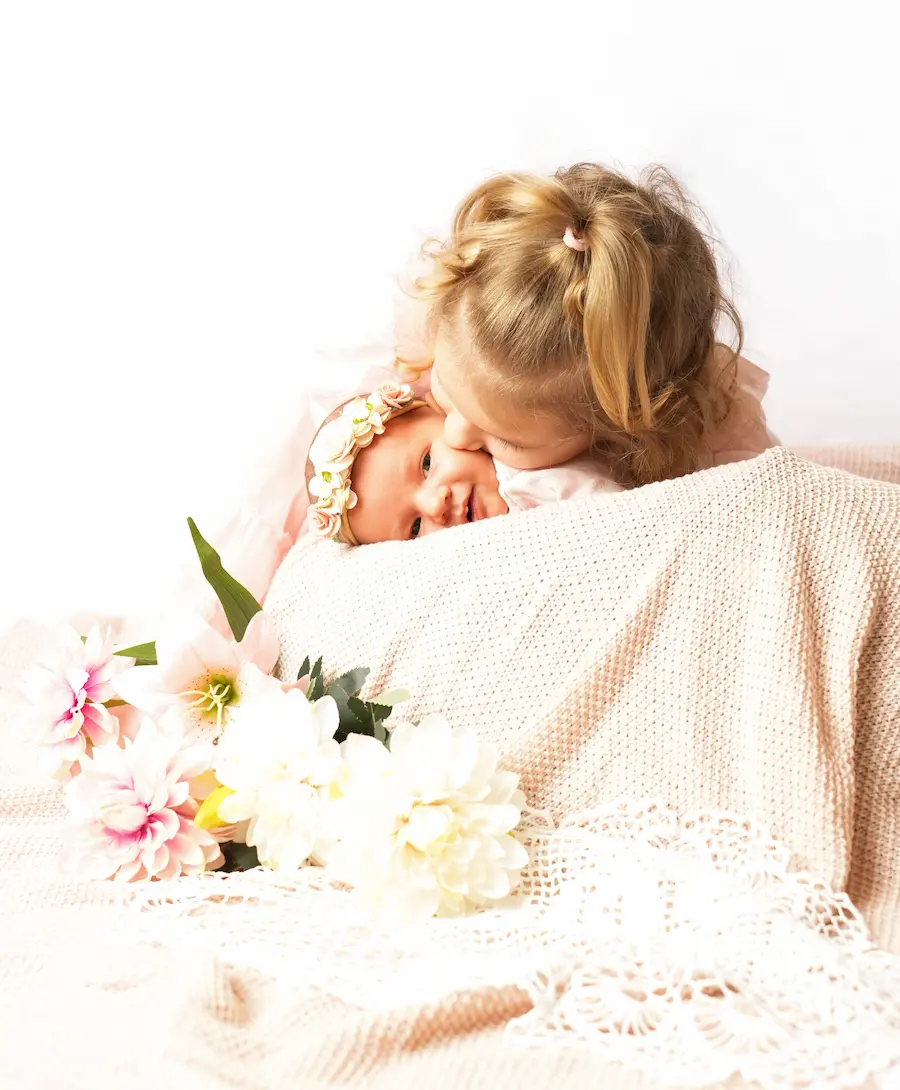 Kleines Mädchen beugt sich über ein Baby mit Blumenstirnband und küsst es