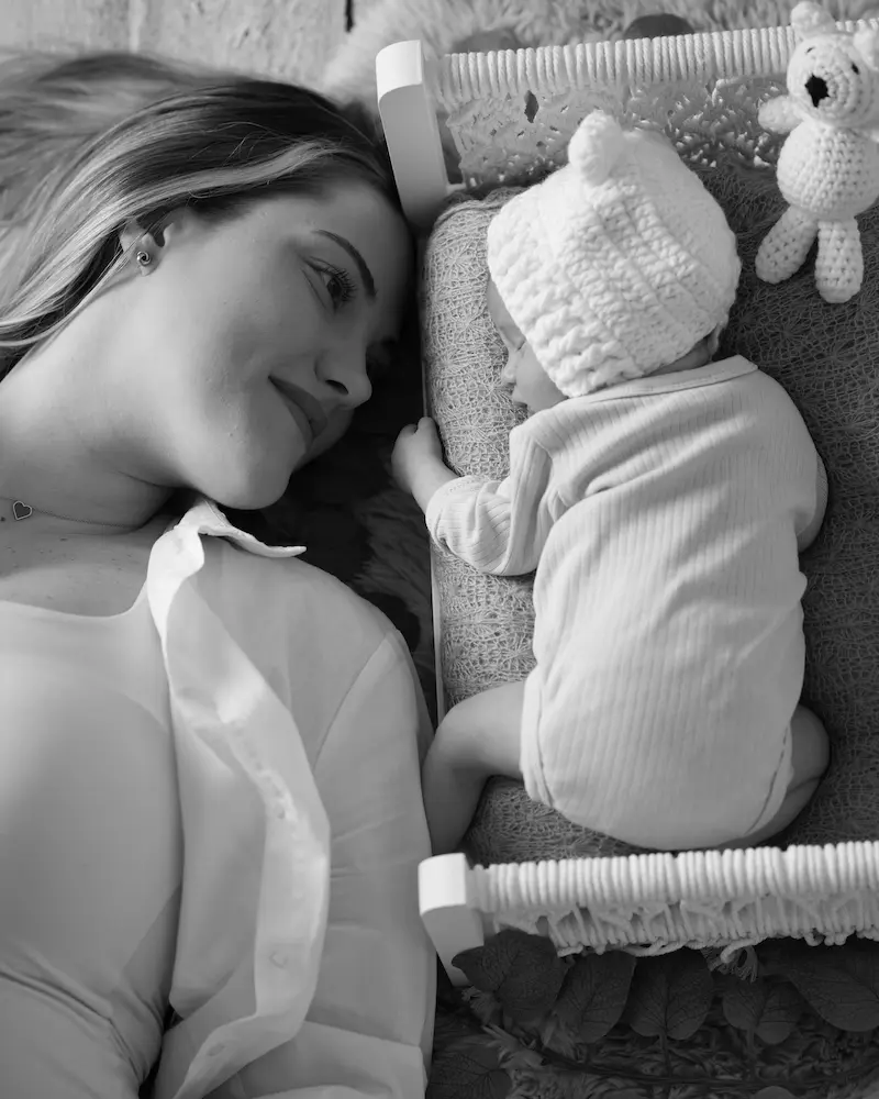 Schwarzweißfoto einer Mutter, die neben dem kleinen Bett ihres schlafenden Babys liegt