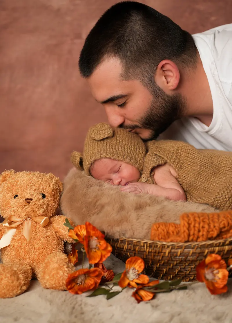 Vater küsst sein Baby mit brauner Strickmütze im weich ausgelegten Korb