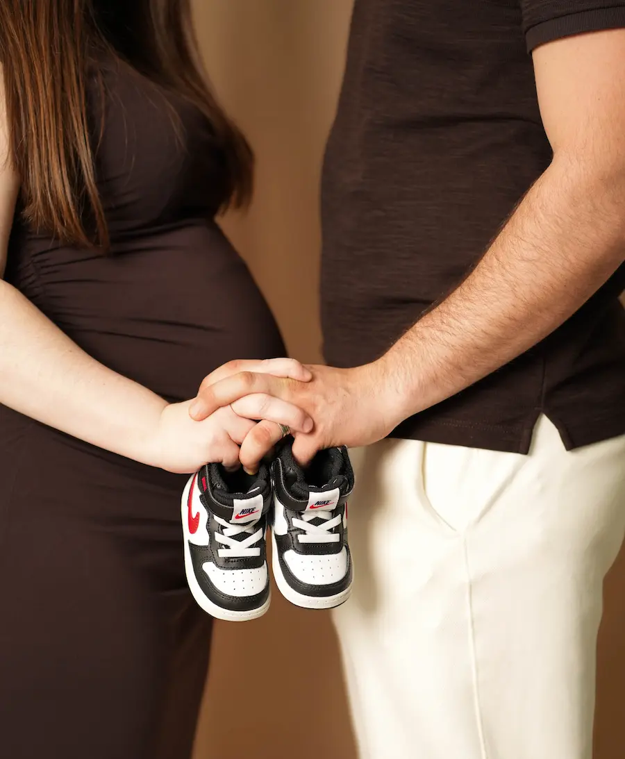Paar hält kleine schwarz-weiße Turnschuhe unter den verschränkten Händen vor dem Babybauch