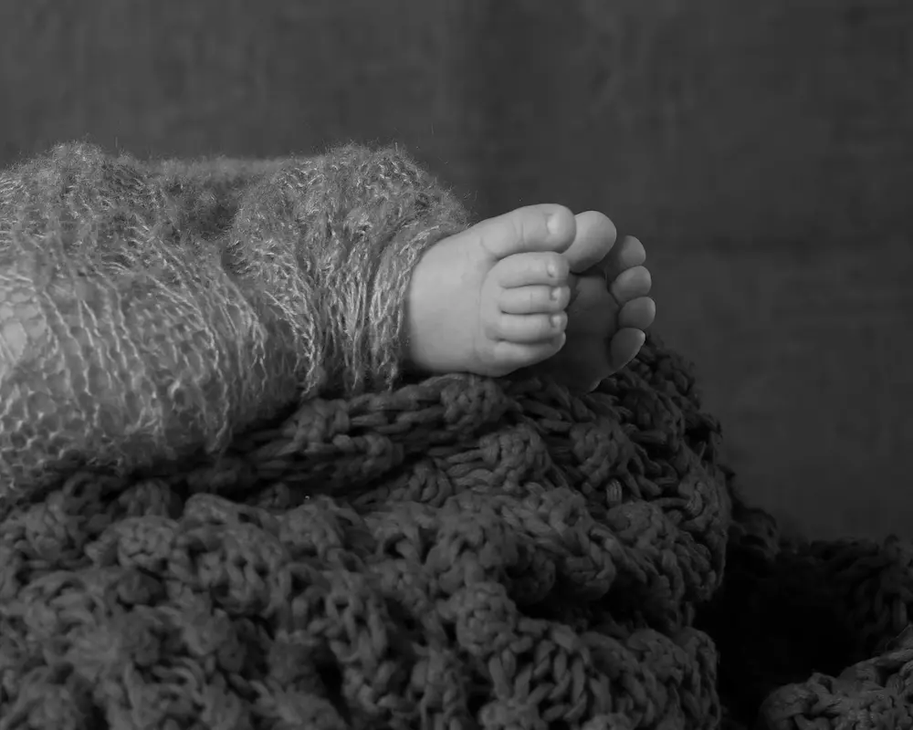Schwarzweißes Detailfoto von Babyfüßen, die aus einer gestrickten Wickeldecke schauen