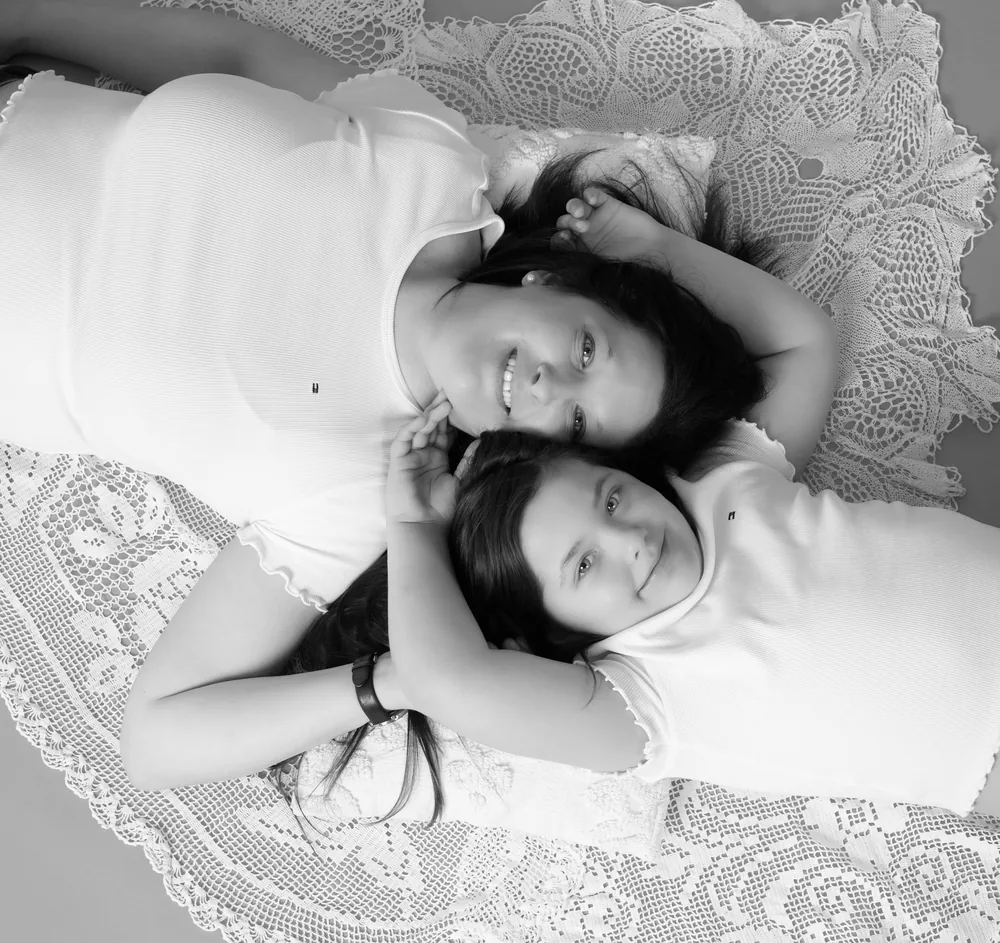 Schwarz-Weiß-Aufnahme von Frau und Mädchen, die Kopf an Kopf auf einer Spitzendecke liegen