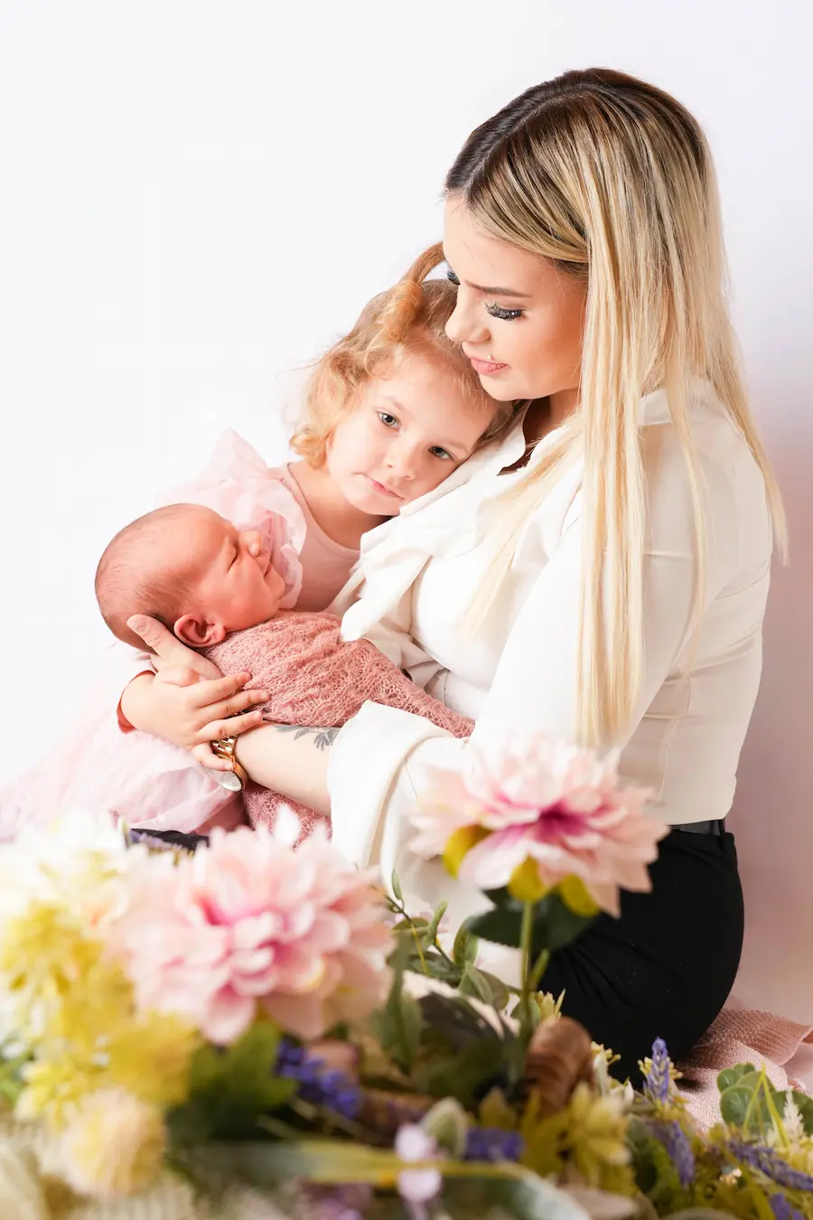 Eine Frau hält ein Baby und ein älteres Kind, mit bunten Blumen im Vordergrund