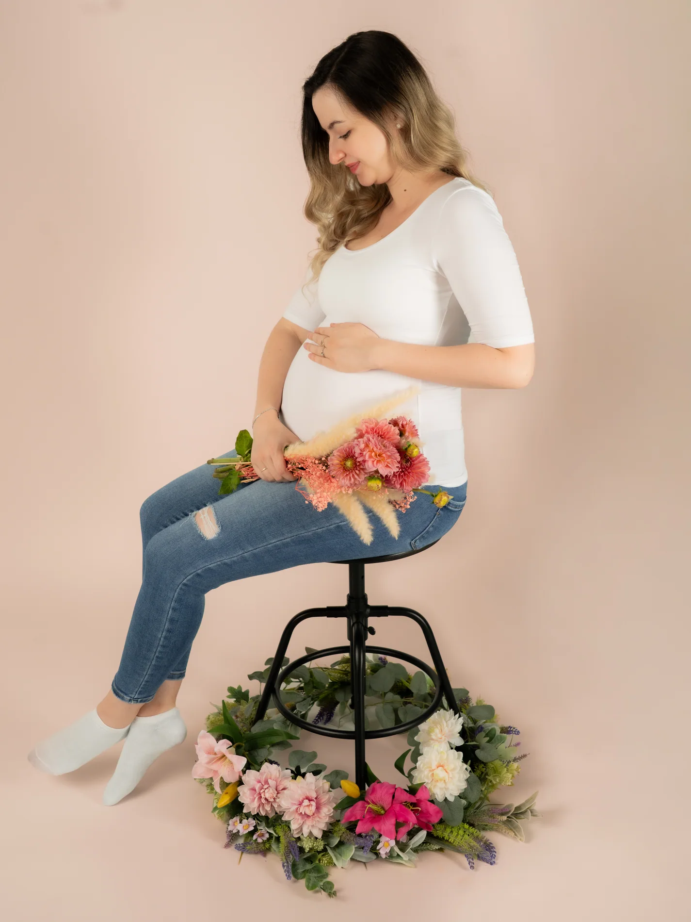 Sitzende Schwangere schaut auf ihren Bauch; ein bunter Strauß liegt auf ihrem Schoß über den Jeans