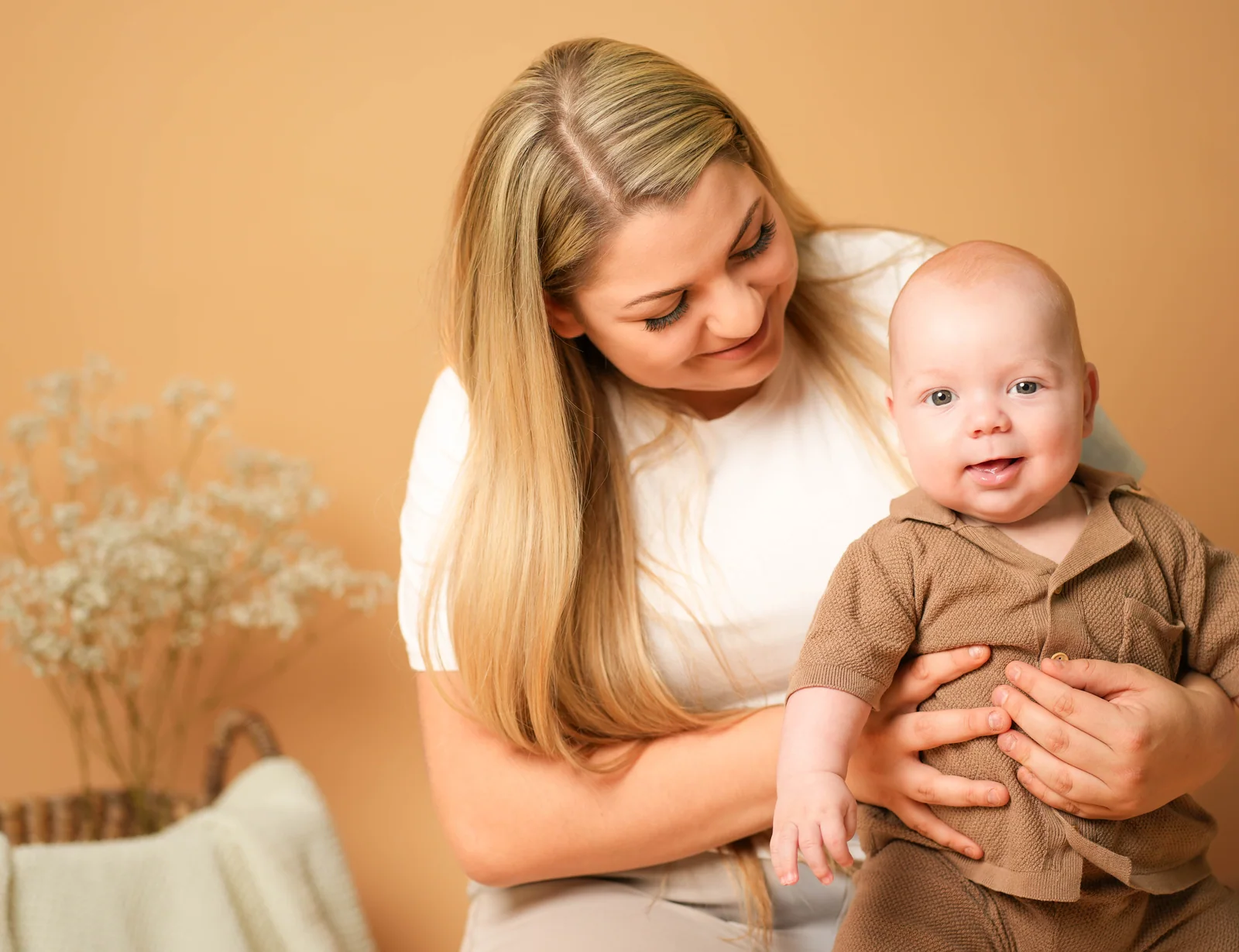 Eine Frau blickt auf das Baby in ihrem Arm, das mit offenem Mund zur Kamera schaut