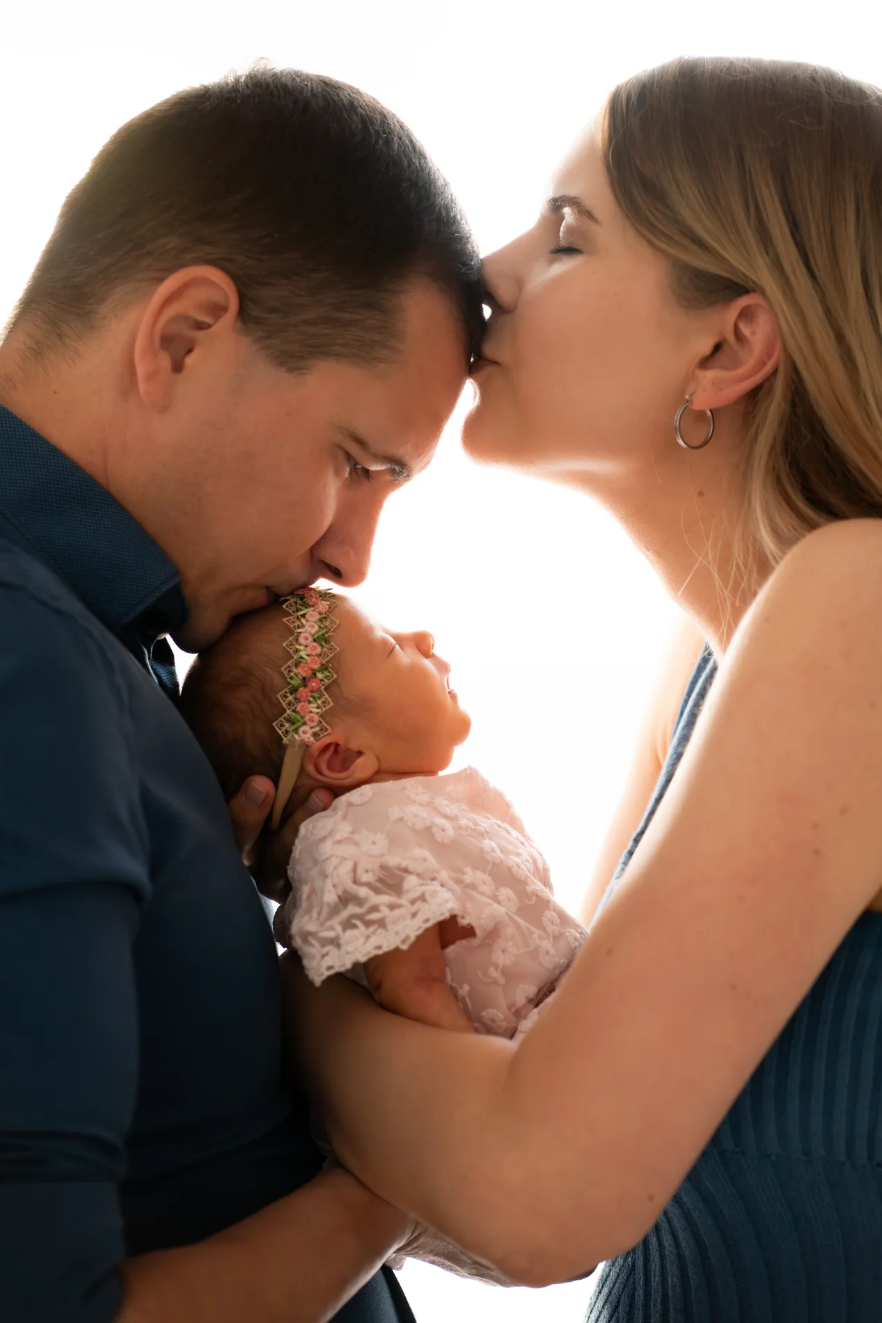 Ein Mann küsst den Kopf eines Babys, während eine Frau seine Stirn küsst