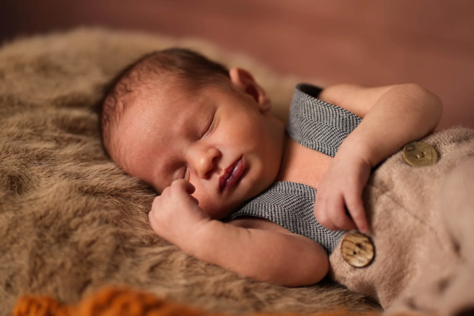 Nahes Babyfoto mit geschlossenen Augen, einer Hand an der Wange und grauen Hosenträgern