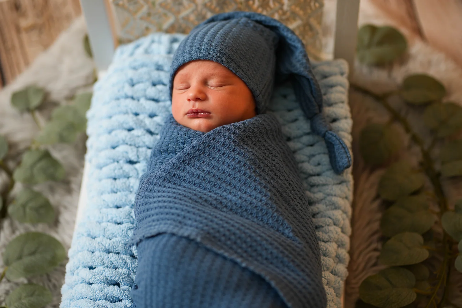 Schlafendes Neugeborenes mit blauer Zipfelmütze, eng in eine blaue Strickdecke gewickelt