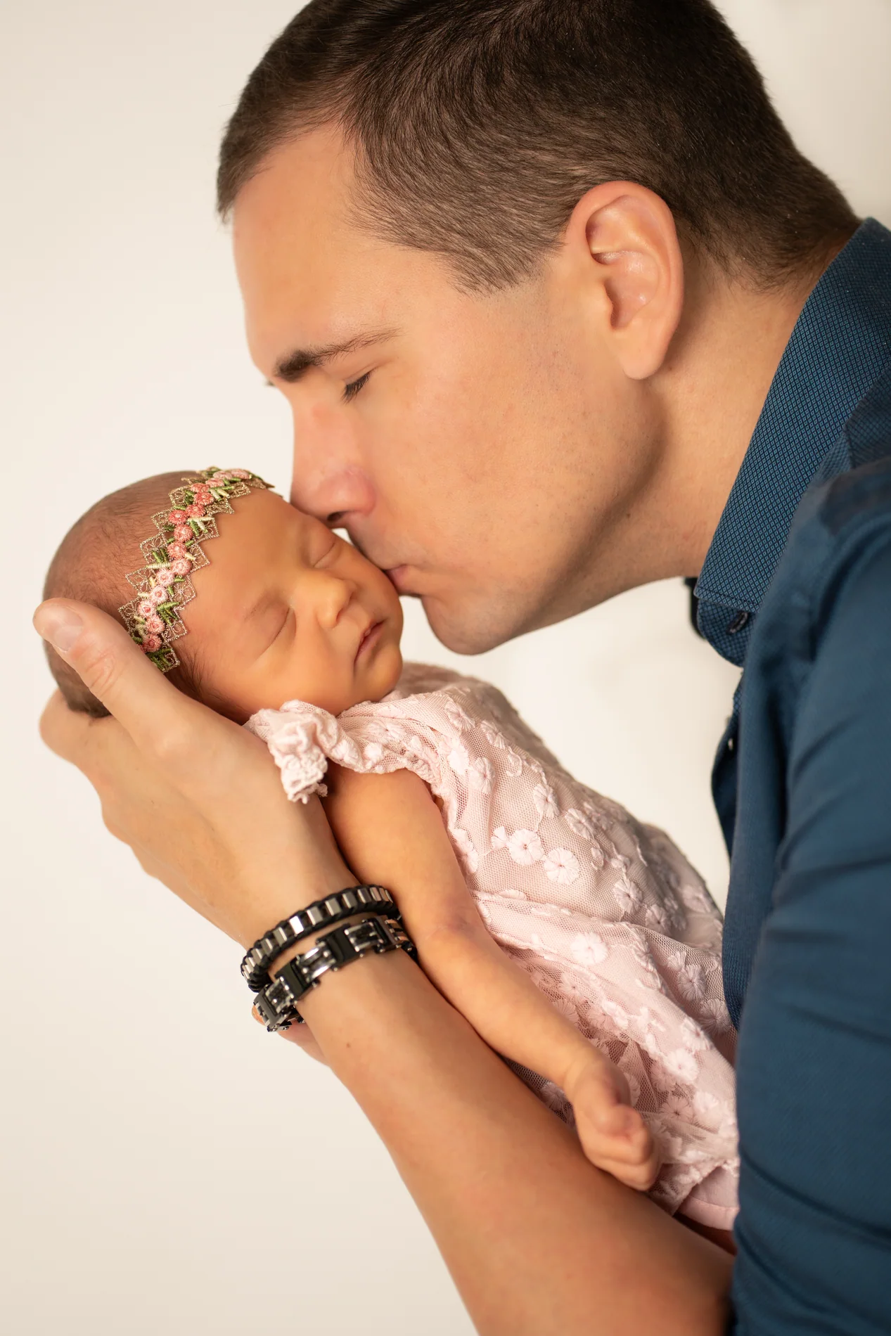 Mann im blauen Hemd küsst ein Baby in rosa Spitze auf die Stirn