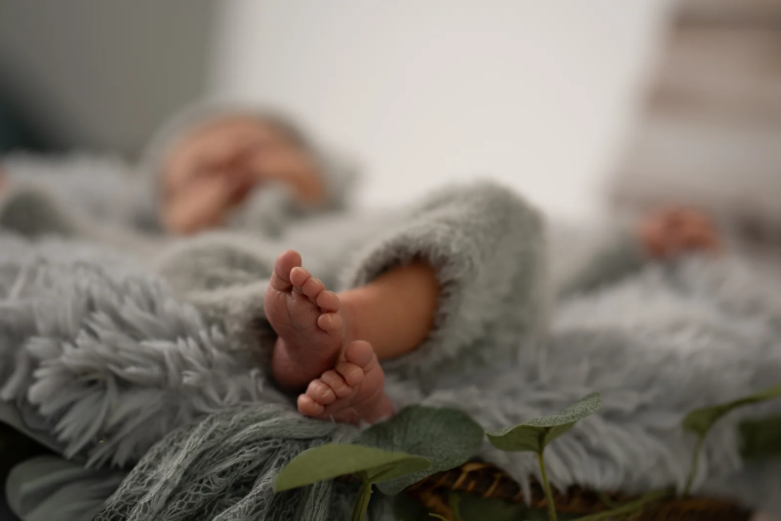 Scharf abgebildete Babyfüße unter einem grauen Strickanzug, während das Gesicht im Hintergrund verschwimmt