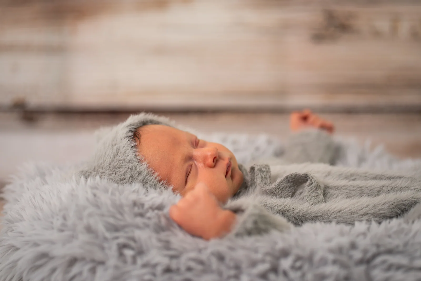 Seitliche Nahaufnahme des schlafenden Babygesichts mit grauer Kapuze und kleiner Faust daneben