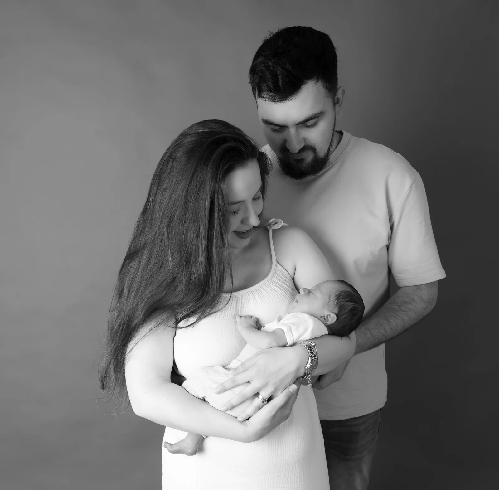 Schwarzweißporträt eines Paares, das gemeinsam auf das Baby in seinen Armen blickt