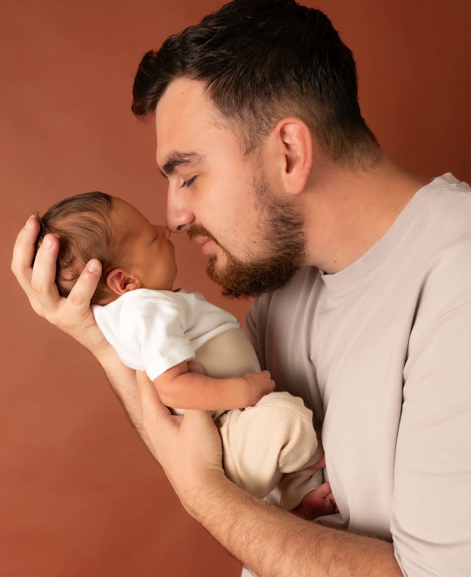 Nahes Porträt eines Mannes, der ein Baby an sein Gesicht hält und dessen Kopf mit einer Hand stützt