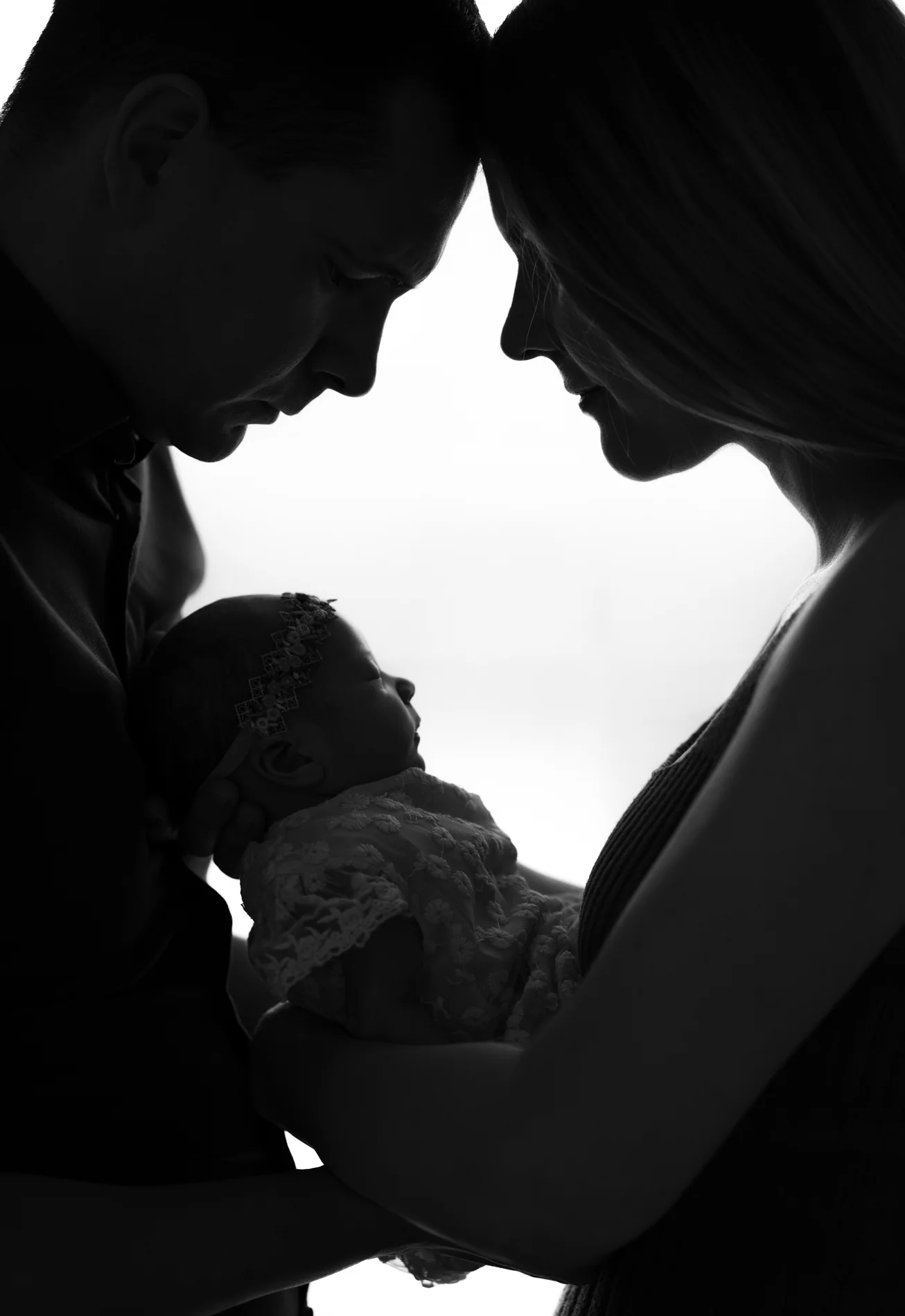 Silhouette eines Paares mit Baby im Gegenlicht, ihre Stirnen berühren sich