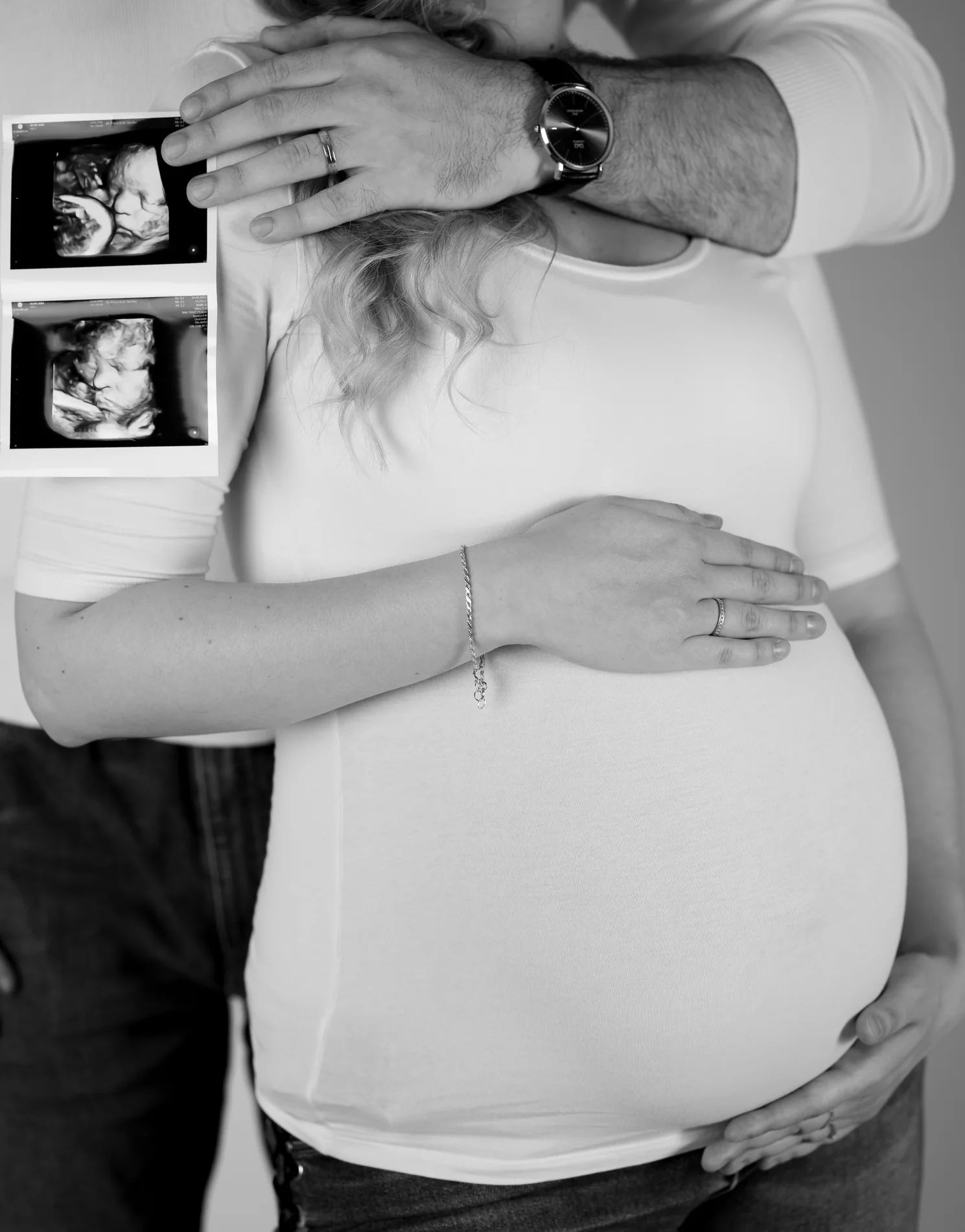 Schwarz-Weiß-Nahaufnahme: Eine Hand hält Ultraschallbilder über dem bekleideten Babybauch