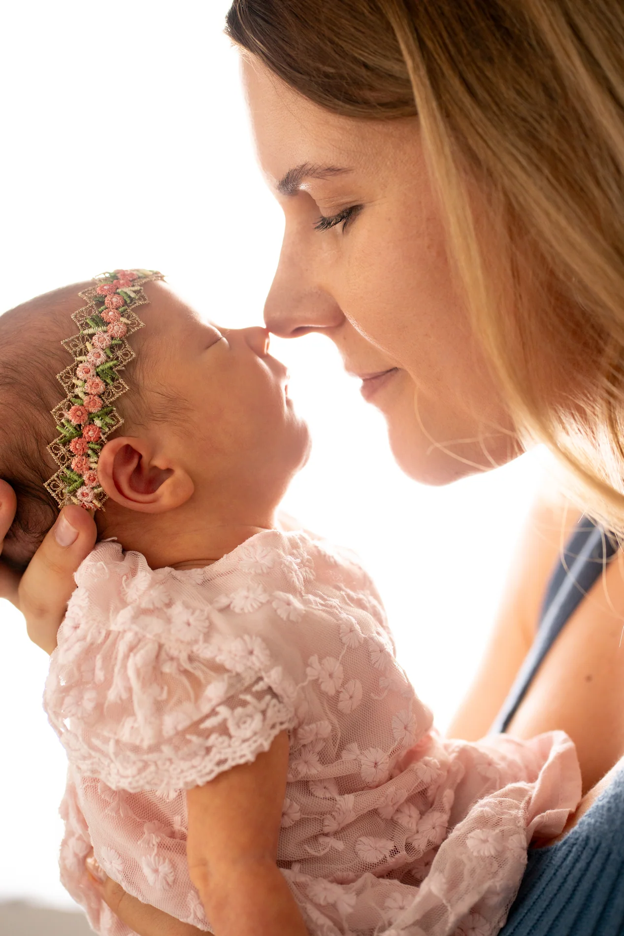 Eine Frau und ein Baby mit Blumenhaarband berühren sich beinahe mit den Nasen