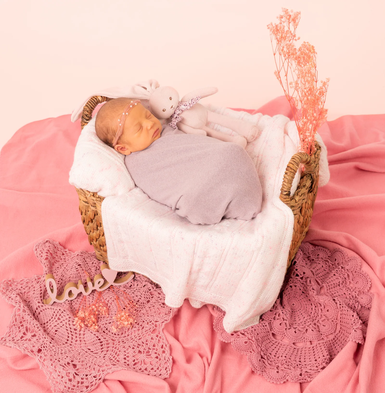 Schlafendes Baby in einem rosafarbenen Korb mit Häschen auf der Decke und Trockenblumen