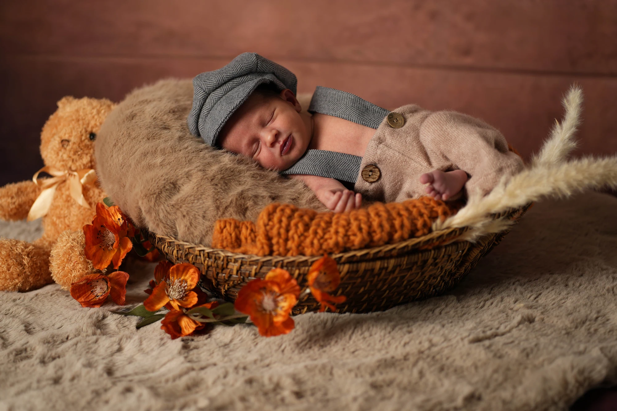 Schlafendes Baby mit grauer Mütze im Flechtkorb, neben ihm ein kleiner Teddy und Herbstblätter